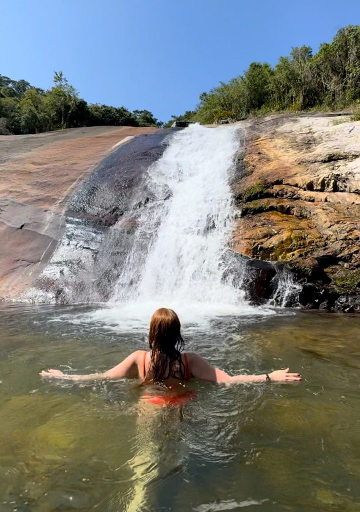 Mulher na água de frente para a cascata da cachoeira